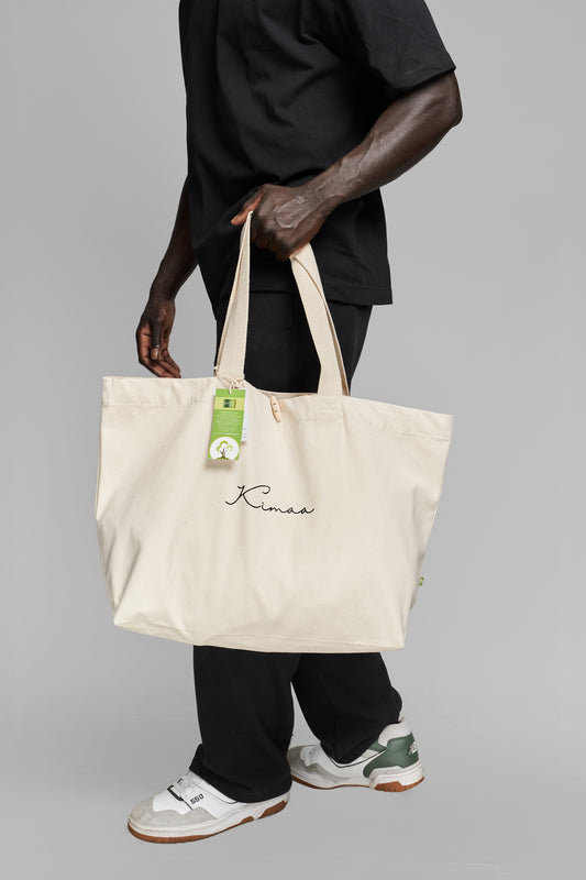Person carrying beige organic cotton tote bag on their side, showcasing Kimaa’s Afro-Nordic streetwear style.